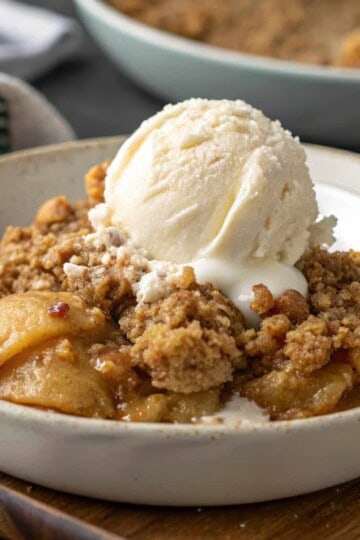 Delicious apple crumble dessert topped with vanilla ice cream in a white bowl, perfect for a sweet treat.