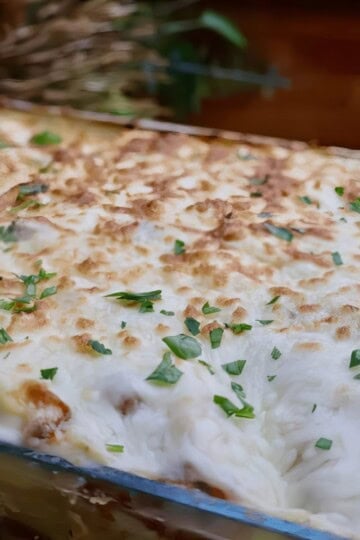 Golden-brown baked pasta bake topped with melted cheese and fresh herbs, served in a glass dish.