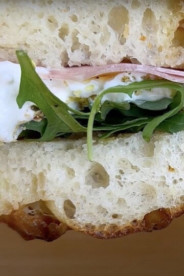 Close-up of a delicious sandwich with ham, arugula, and creamy cheese on fresh, crusty bread. Perfect lunch option.
