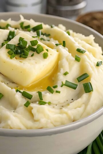 Creamy mashed potatoes topped with melting butter and fresh chives in a white bowl.