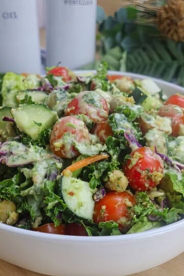Fresh garden salad with cherry tomatoes, cucumber, kale, and creamy dressing in a white bowl on a wooden table.