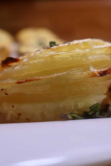 Close-up of a crispy, layered potato stack garnished with herbs on a white plate.