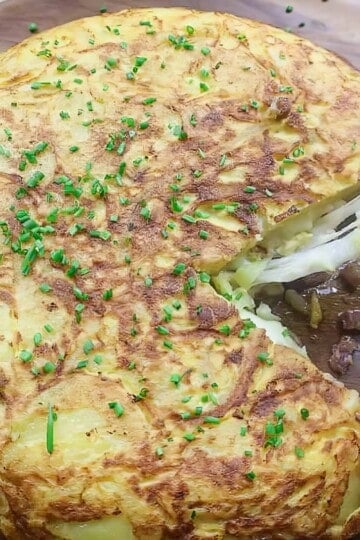 Delicious Spanish omlette with chives on a wooden board, showcasing a sliced portion.
