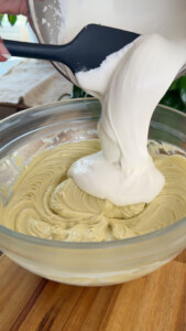 Pouring creamy batter into a bowl with pistachio mix.