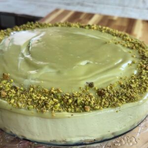 Creamy no bake pistachio cake with a smooth green frosting and crushed pistachio topping on a wooden board.