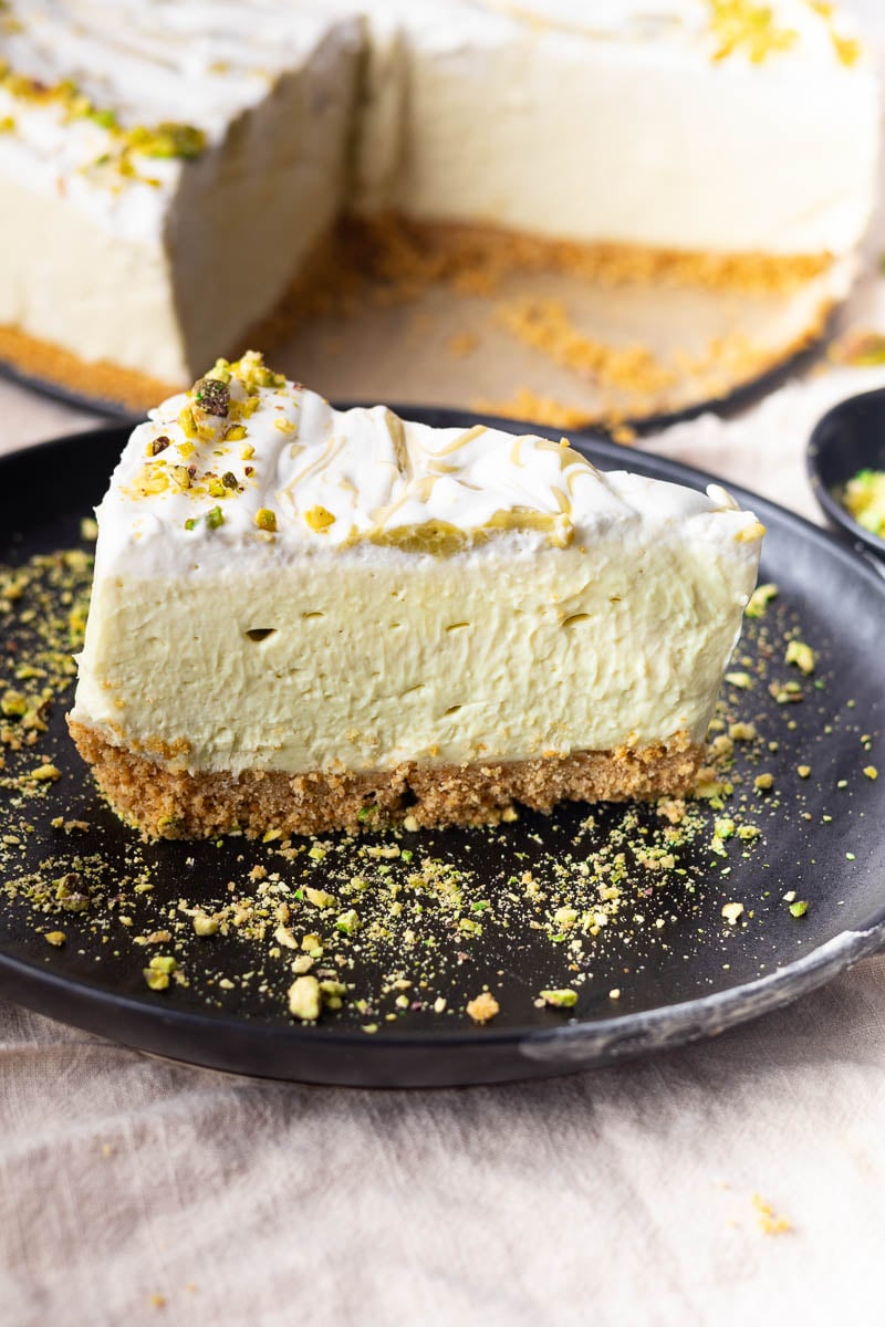 No-bake pistachio mascarpone cheesecake topped with crushed pistachios on a black plate.