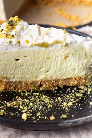 No-bake pistachio mascarpone cheesecake on a black plate with crumbly crust and nut garnish.