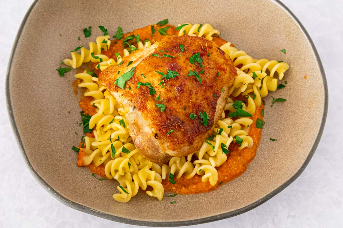 Crispy chicken romesco with fusilli pasta  in a beige bowl. 