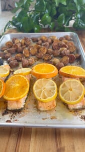 Roasted salmon with orange slices, accompanied by seasoned potatoes on a baking tray.