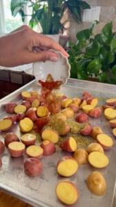Seasoning baby potatoes on a baking sheet with spices.