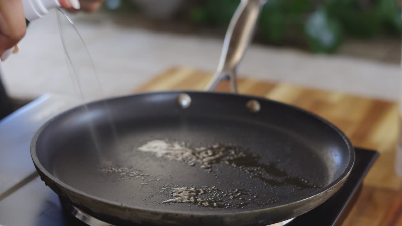 Pouring oil into a black frying pan on a kitchen stove for cooking preparation.