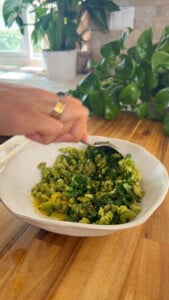 Mixing chopped greens and herbs in a white bowl on a wooden countertop.