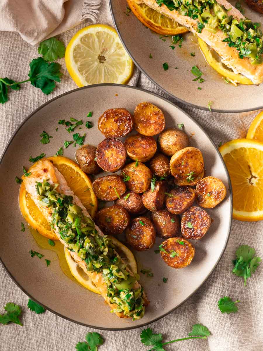 Orange salmon with citrus-olive gremolata and roasted potatoes garnished with citrus slices on a plate.
