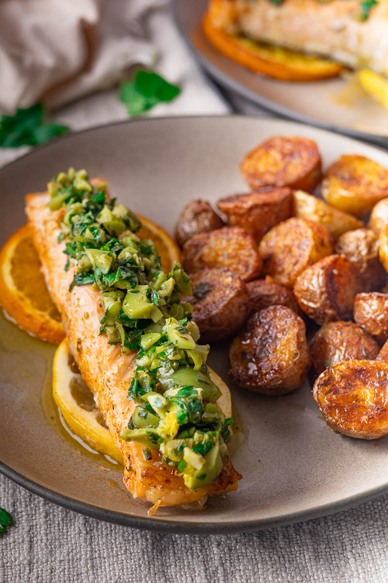 Orange Salmon with Citrus-Olive Gremolata with herb topping on orange slices, served with roasted potatoes on a gray plate.