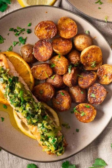 Baked salmon with Orange Salmon with Citrus-Olive Gremolata and roasted potatoes on a plate with citrus garnish.
