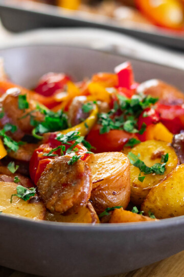 Delicious roasted sausage, peppers, and potatoes and herbs in a serving dish.