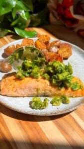 Grilled salmon with herbs and roasted potatoes on a plate, garnished with fresh greens.