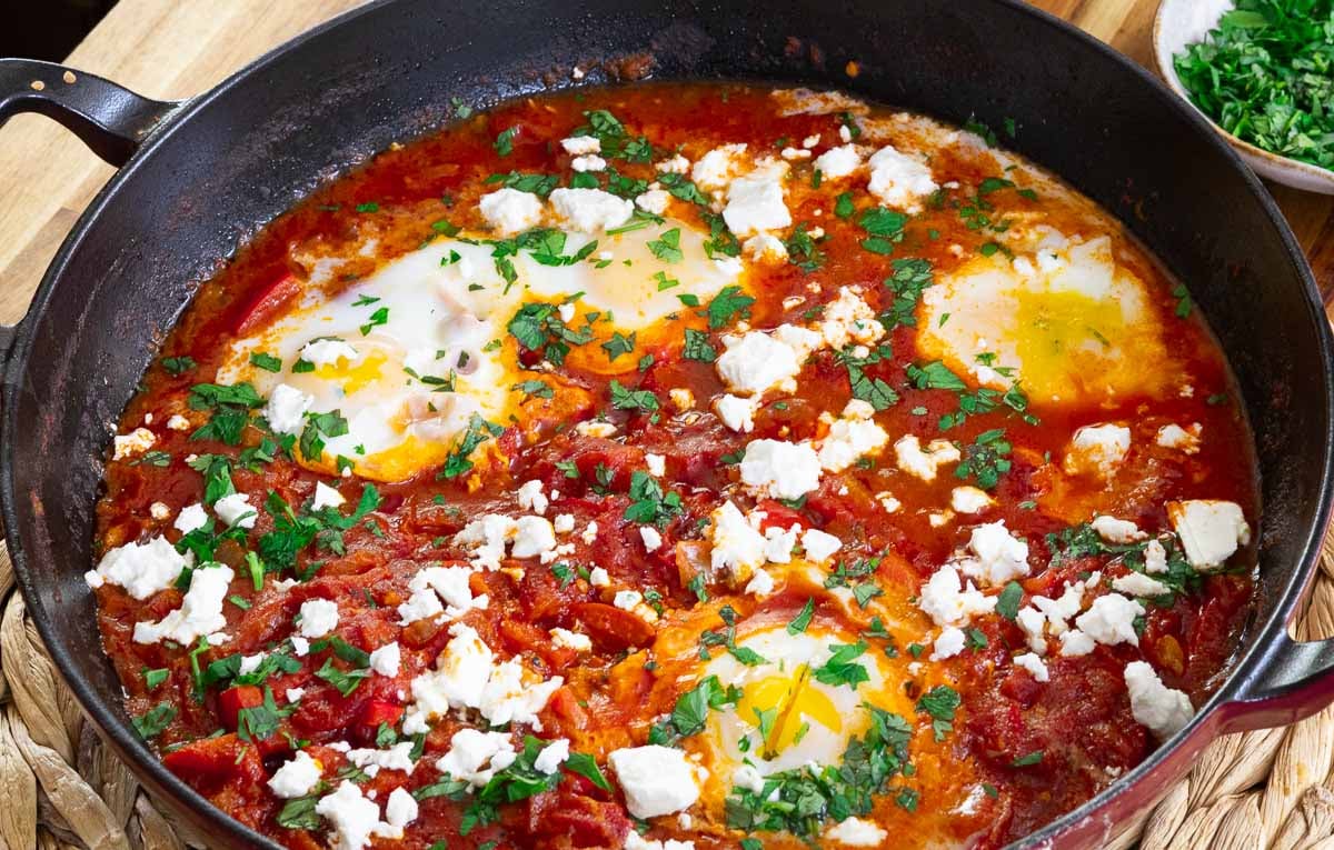 Savory Shakshuka in skillet with poached eggs, tomatoes, feta, and herbs. Perfect for a delicious breakfast or brunch.