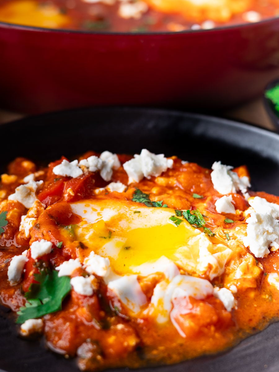 Shakshuka with poached egg, feta cheese, and herbs in tomato sauce on a black plate.