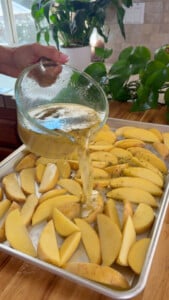 Pouring sauce over sliced potatoes on a baking sheet.
