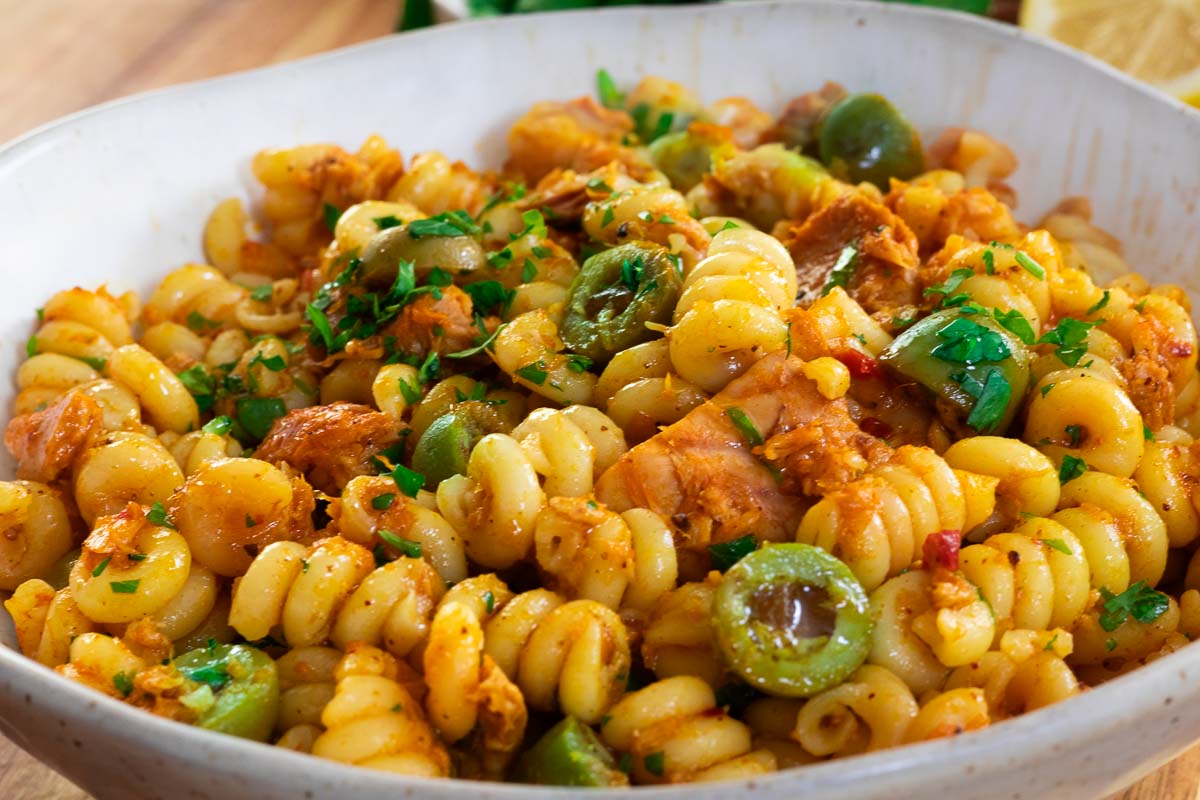 Delicious spirali pasta with olives, chicken, herbs, and spices in a white bowl, perfect for a savory meal.