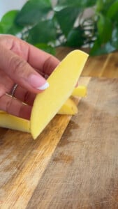 Woman holding cut potato over wooden cutting board.