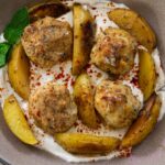 Meatballs and roasted potatoes on yogurt sauce with herbs in a bowl.