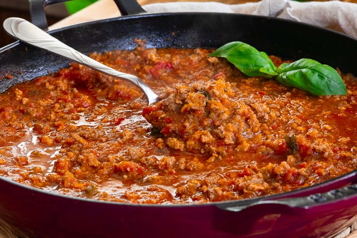 Rich homemade hidden veggie pasta sauce in a skillet with a serving spoon and fresh basil garnish.