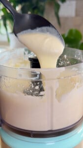 Whipped feta being poured from a spoon into a food processor bowl.