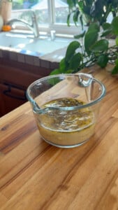 Glass measuring cup with sauce on wooden kitchen counter.