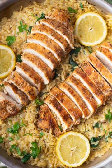 Sliced roasted chicken breast on creamy orzo pasta with lemon slices and parsley garnish.