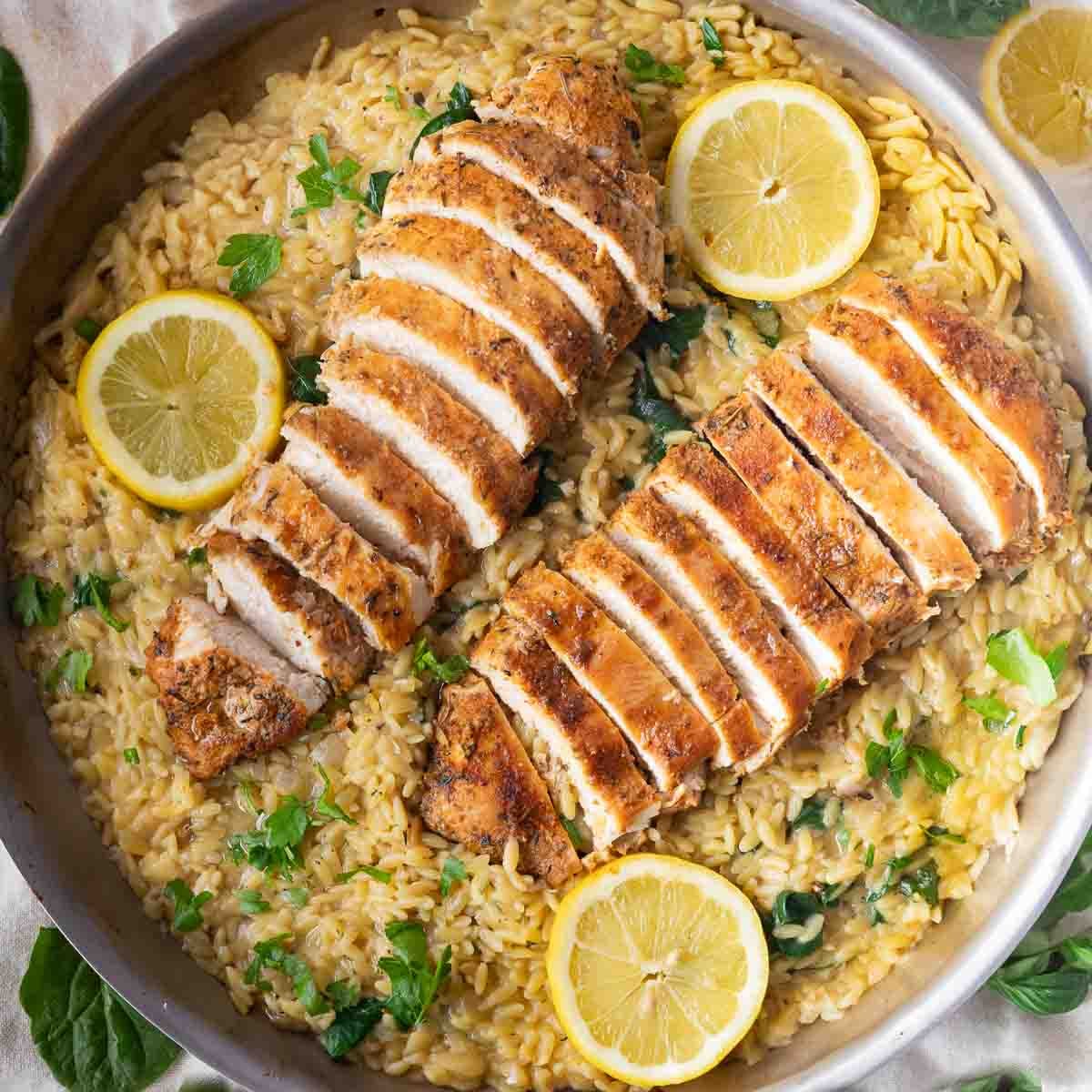 Sliced roasted chicken breast on creamy orzo pasta with lemon slices and parsley garnish.