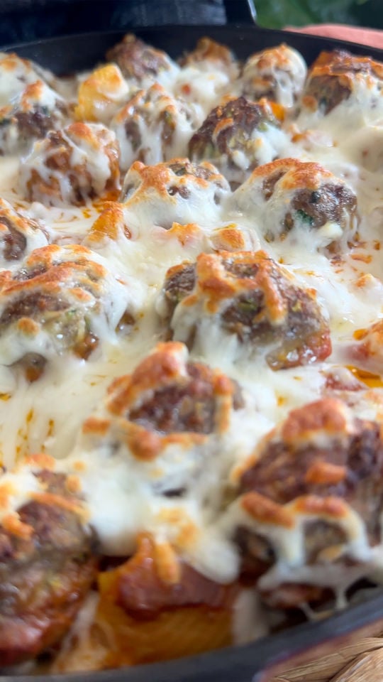 Baked meatballs covered in melted cheese on a bed of pasta in a black skillet.
