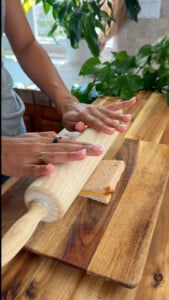 Hands rolling bread on a wooden cutting board.