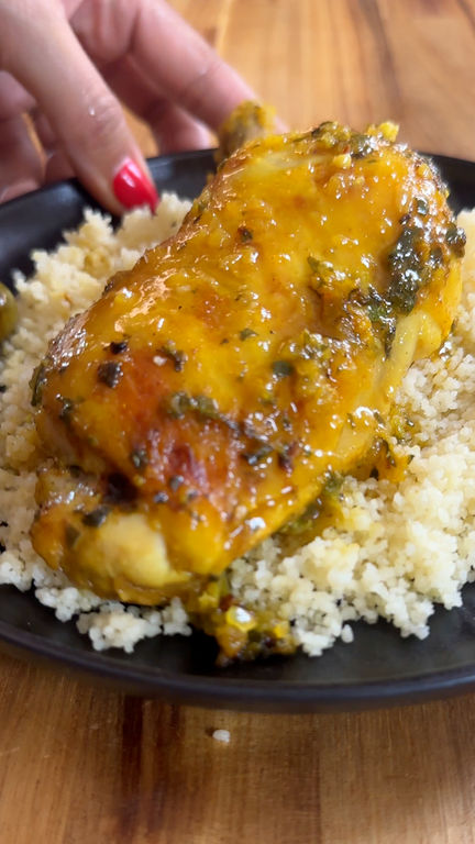 Chicken with sauce on couscous, served on a black plate, being gently placed by a hand.