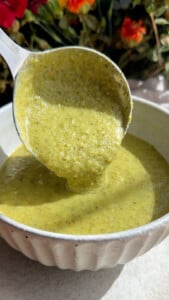 Ladle pouring green soup into a white bowl.