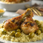 Moroccan lemon chicken and olives served on a bed of couscous, garnished with spices.