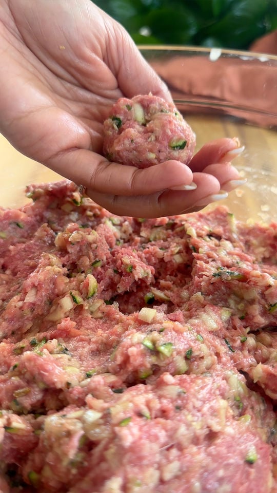Hand shaping meatball with minced meat mixture in a glass bowl.