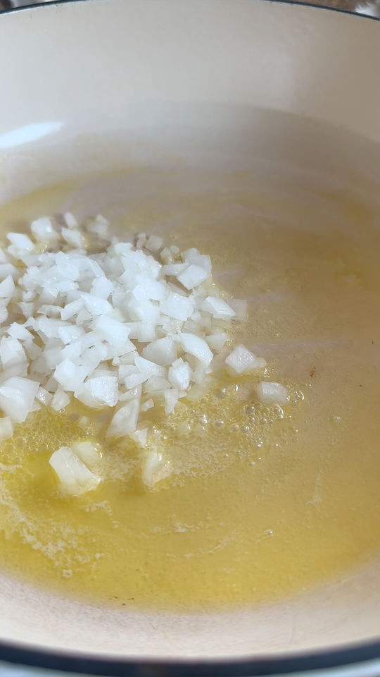 Chopped onions sautéing in melted butter in a white pan.