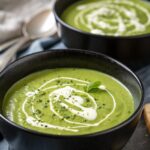 Sheet Pan Broccoli Zucchini Soup garnished with cream and herbs in a black bowl.