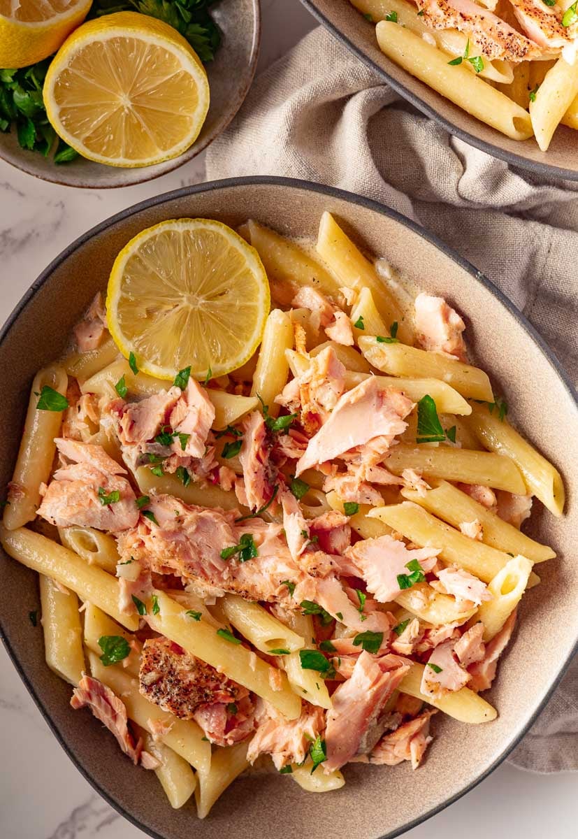 Pasta alla Salmone with lemon slices, and parsley in a bowl, on a table with sliced lemons and greens.