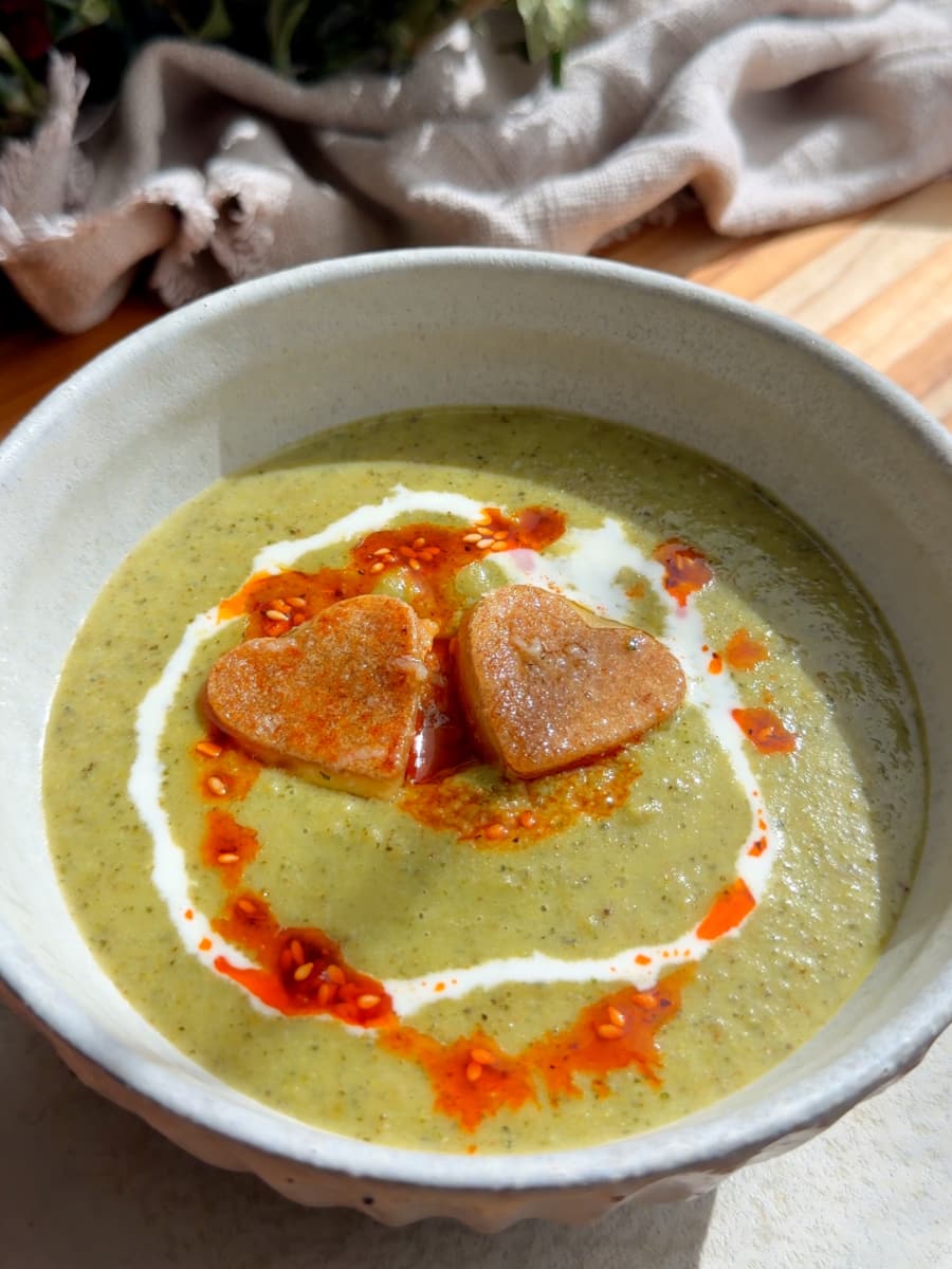 Creamy green soup topped with heart-shaped croutons, cream, and chili oil.