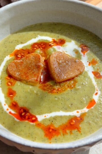 Creamy green soup topped with heart-shaped croutons, cream, and red chili oil.