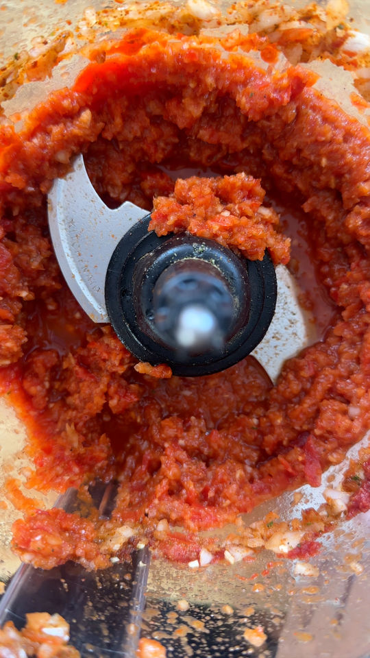 Close-up of a food processor blending red tomato and garlic mixture.