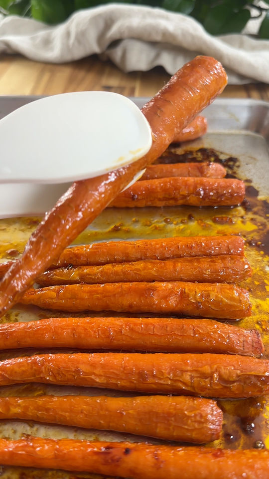 Roasted carrots being picked up with a white spatula on a baking sheet.
