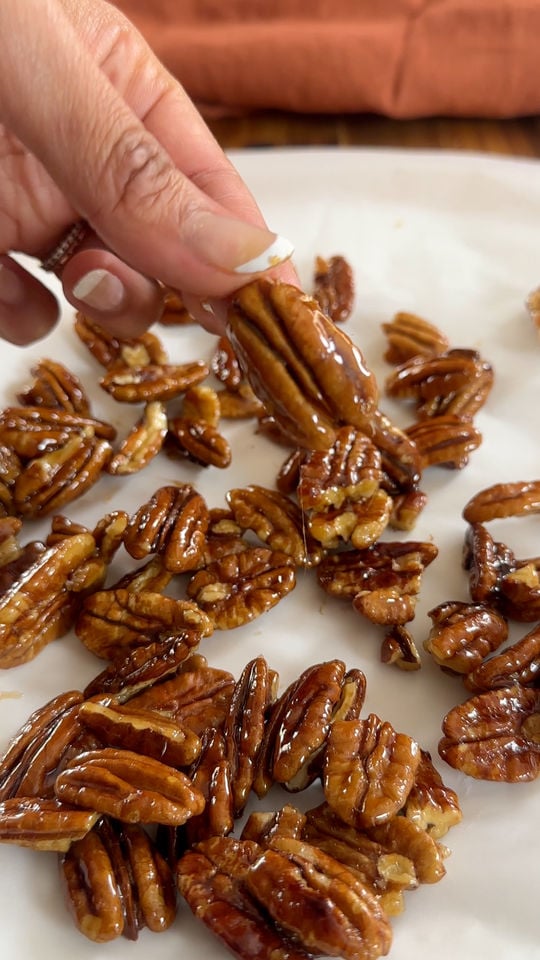 Hand holding glazed pecan over a tray of glazed pecans.