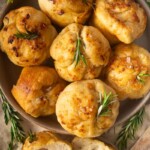 Focaccia muffins with rosemary on a plate, surrounded by fresh rosemary sprigs.