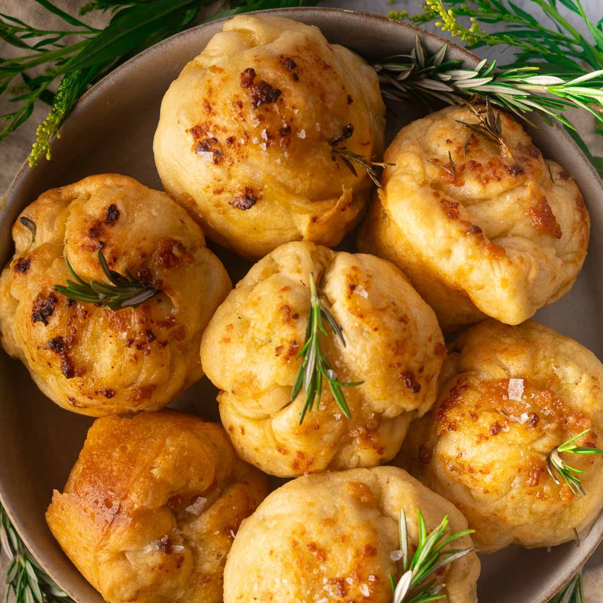 Focaccia muffins topped with rosemary in a bowl.