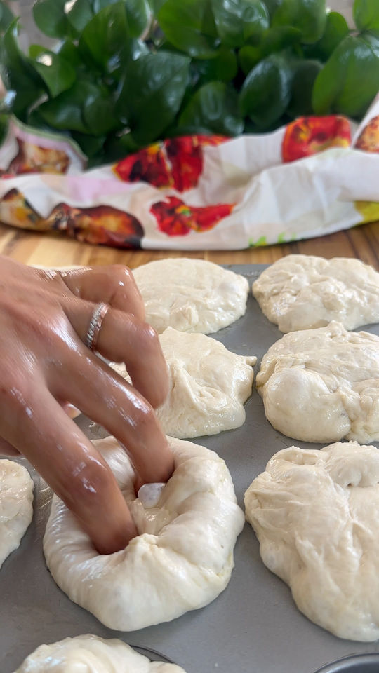 Hand shaping dough balls on a tray with leaves and a colorful cloth in the background.