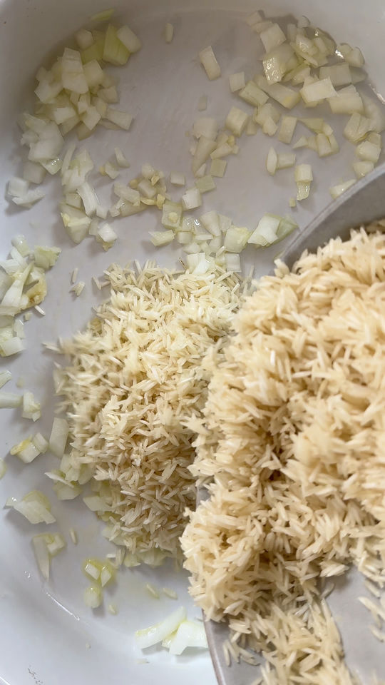 Chopped onions and uncooked rice in a white pot, prepped for cooking.